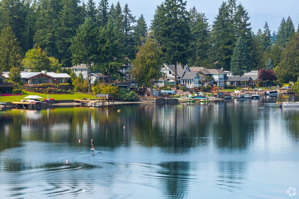 A peaceful lakeside neighborhood in Black Diamond with houses, docks, trees, and a person paddleboarding on calm water—ideal for those seeking serenity and reliable plumbing services in Black Diamond. Plumbers in Black Diamond, WA