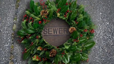 A holiday wreath decorated with pinecones and red berries resting on a metal sewer cover that may require drain cleaning and repair. Plumbers in Black Diamond, WA